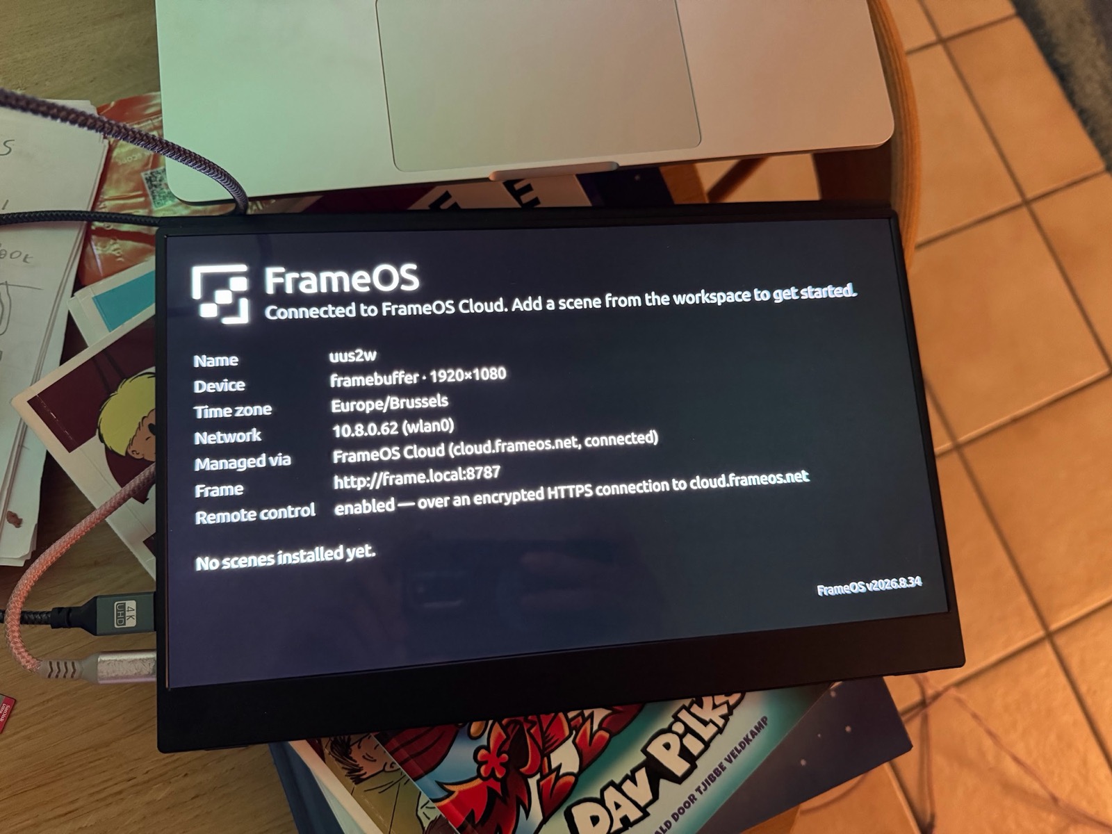 A portable HDMI monitor showing the FrameOS welcome screen from a Raspberry Pi